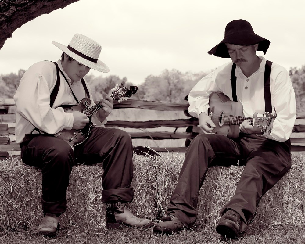 Two men dressed in historic period clothing with guitars.