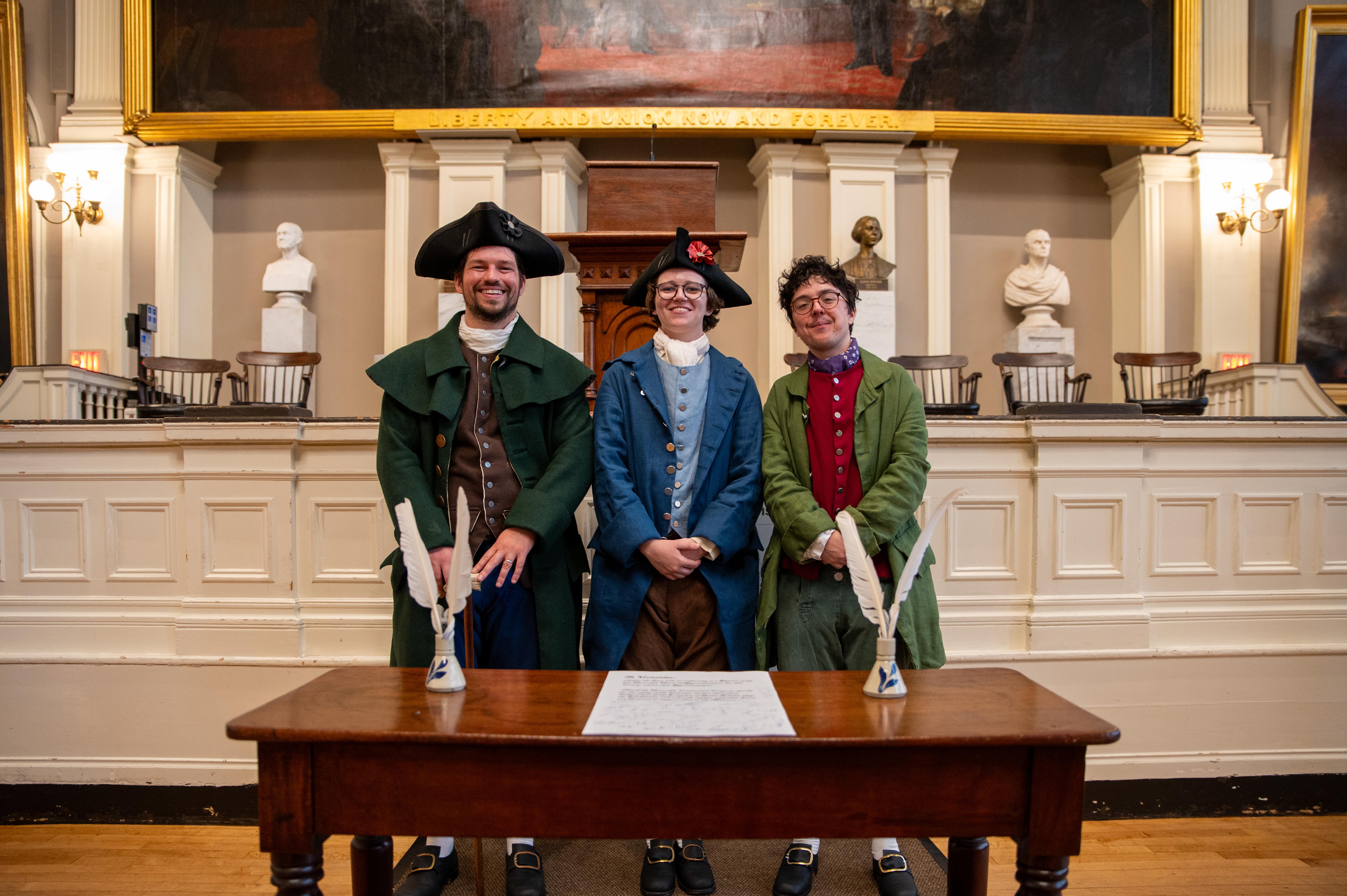 Three rangers in historic clothing stand in front of a signed resolution smiling at the camera