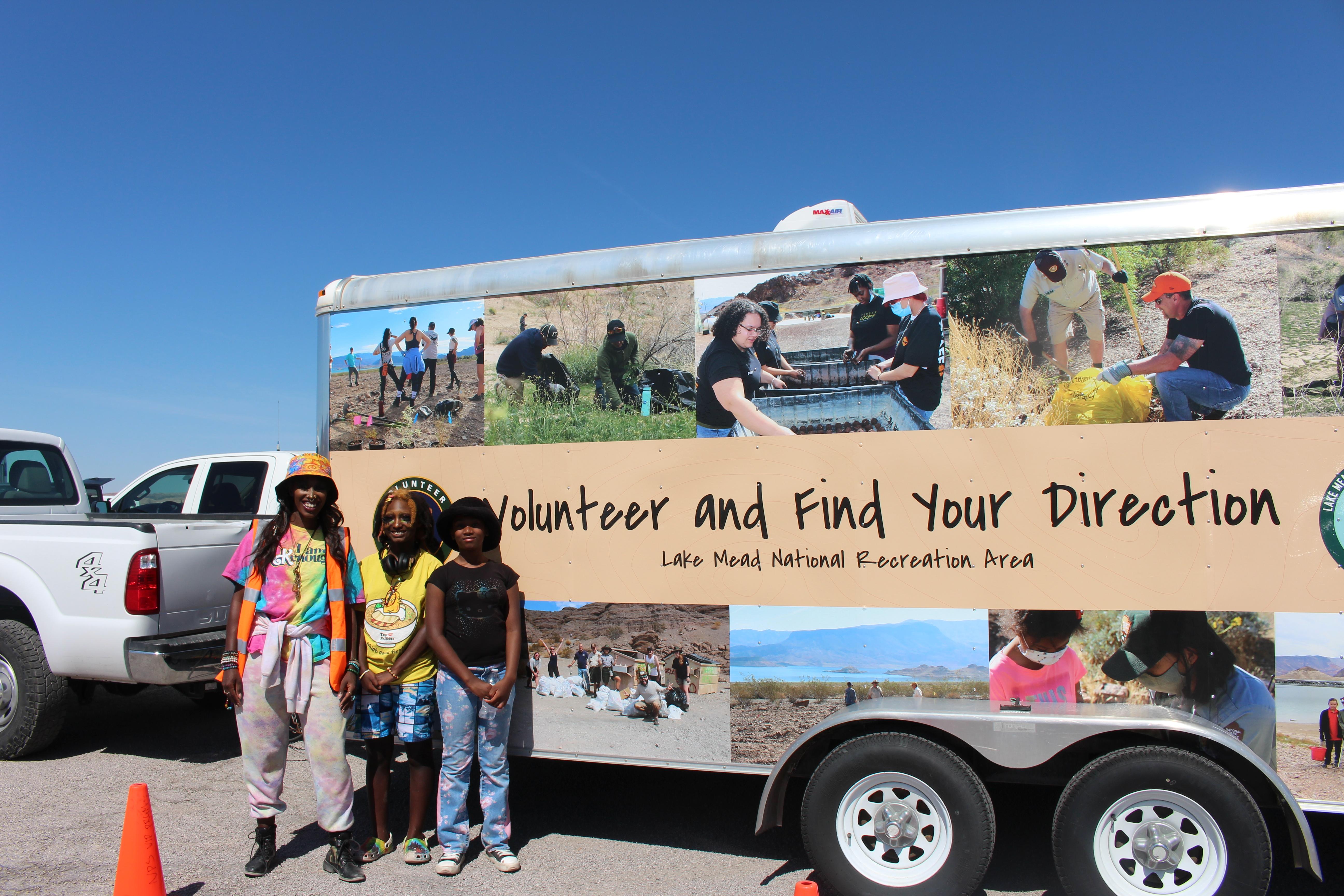 Volunteers standing in front of colorful trailer that reads "Volunteer and Find Your Direction"