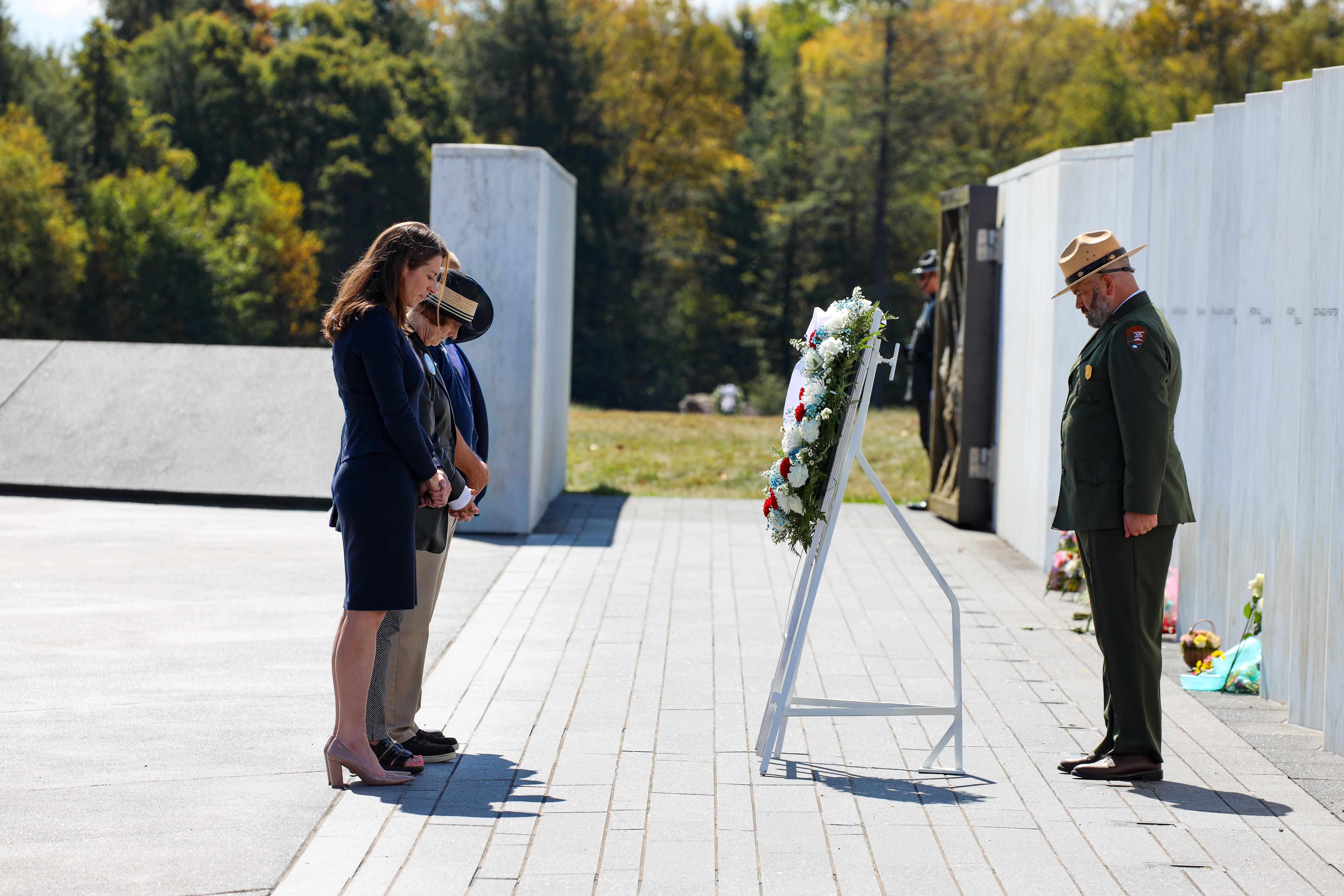 A group of individuals stand with heads bowed in front of a wreath at the Wall of Names.