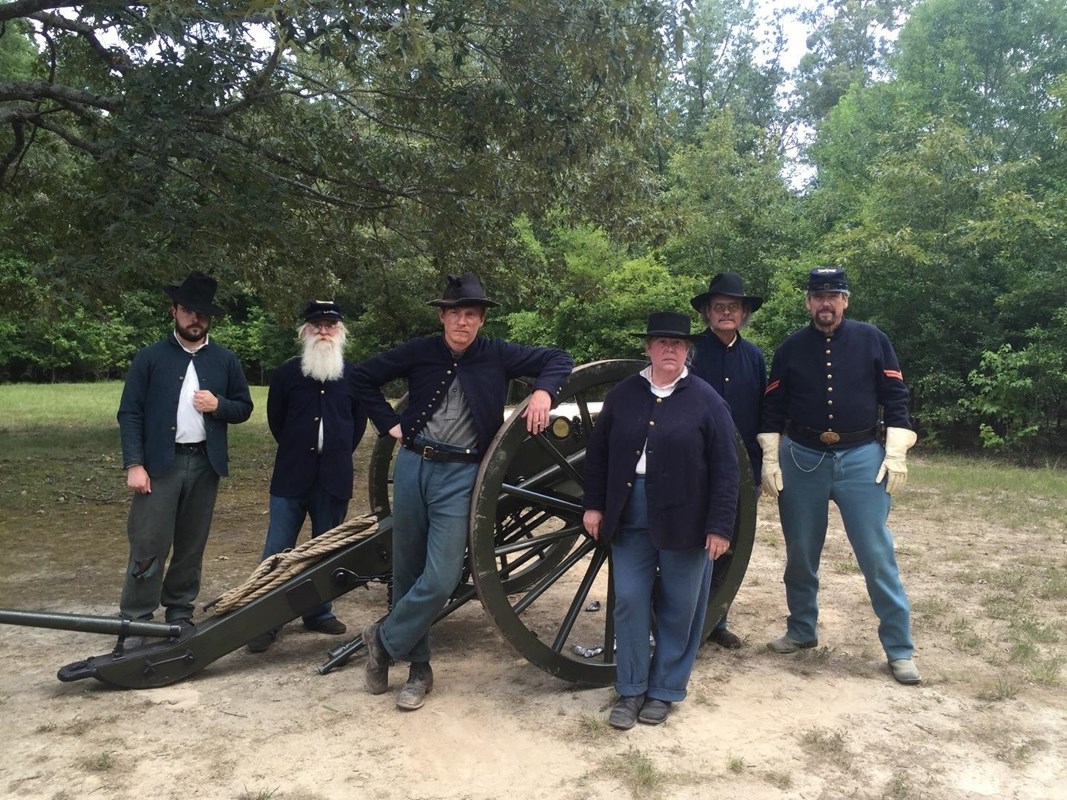 Several living historians in blue uniforms pose around a bronze cannon