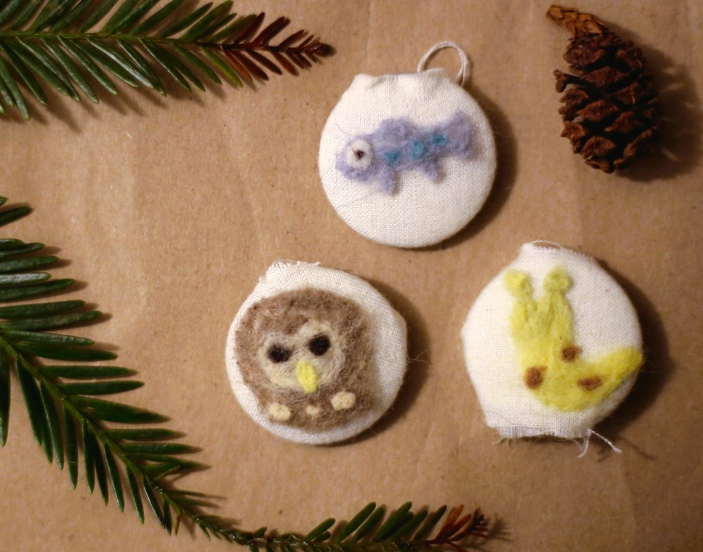 three felt buttons with an owl, fish, and banana slug on a brown paper background