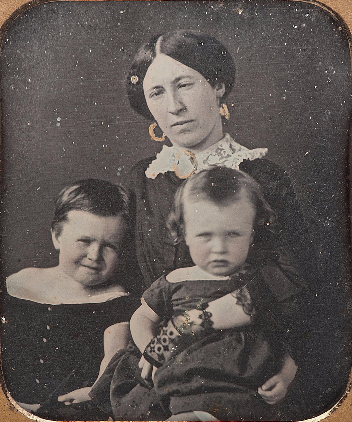 Old photograph of a young woman with dark hair seating and holding two young children