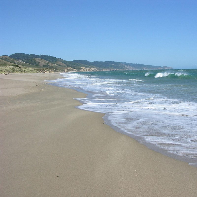 A sandy beach on the left with small ocean waves washing in from the right.