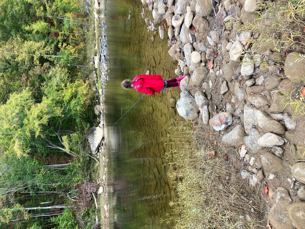 Youth in red jacket fishing along the river bank.