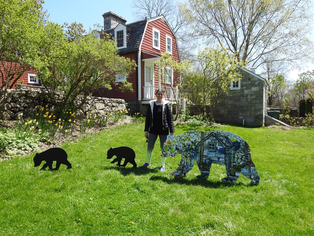 A woman stands in front of a large bear designed with a painting of a tool shed.