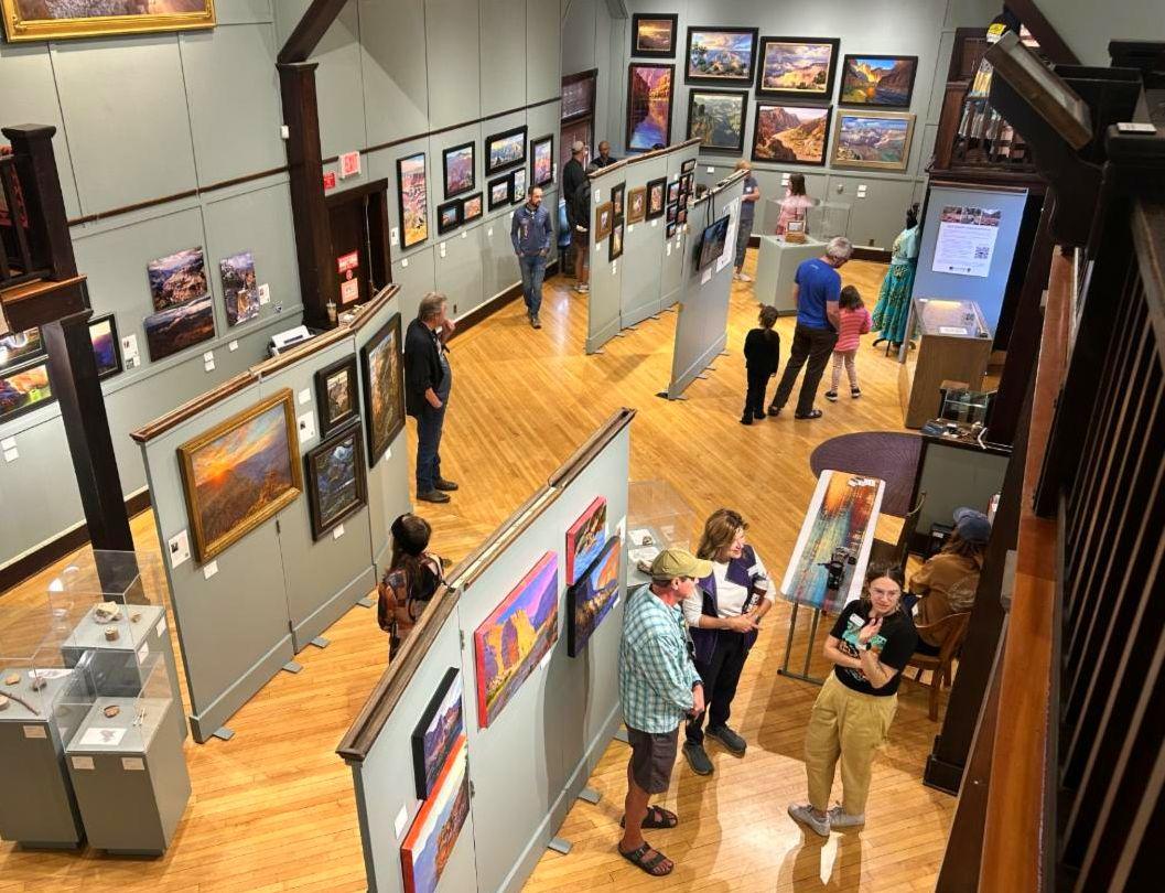several people are viewing paintings of Grand Canyon in an art gallery