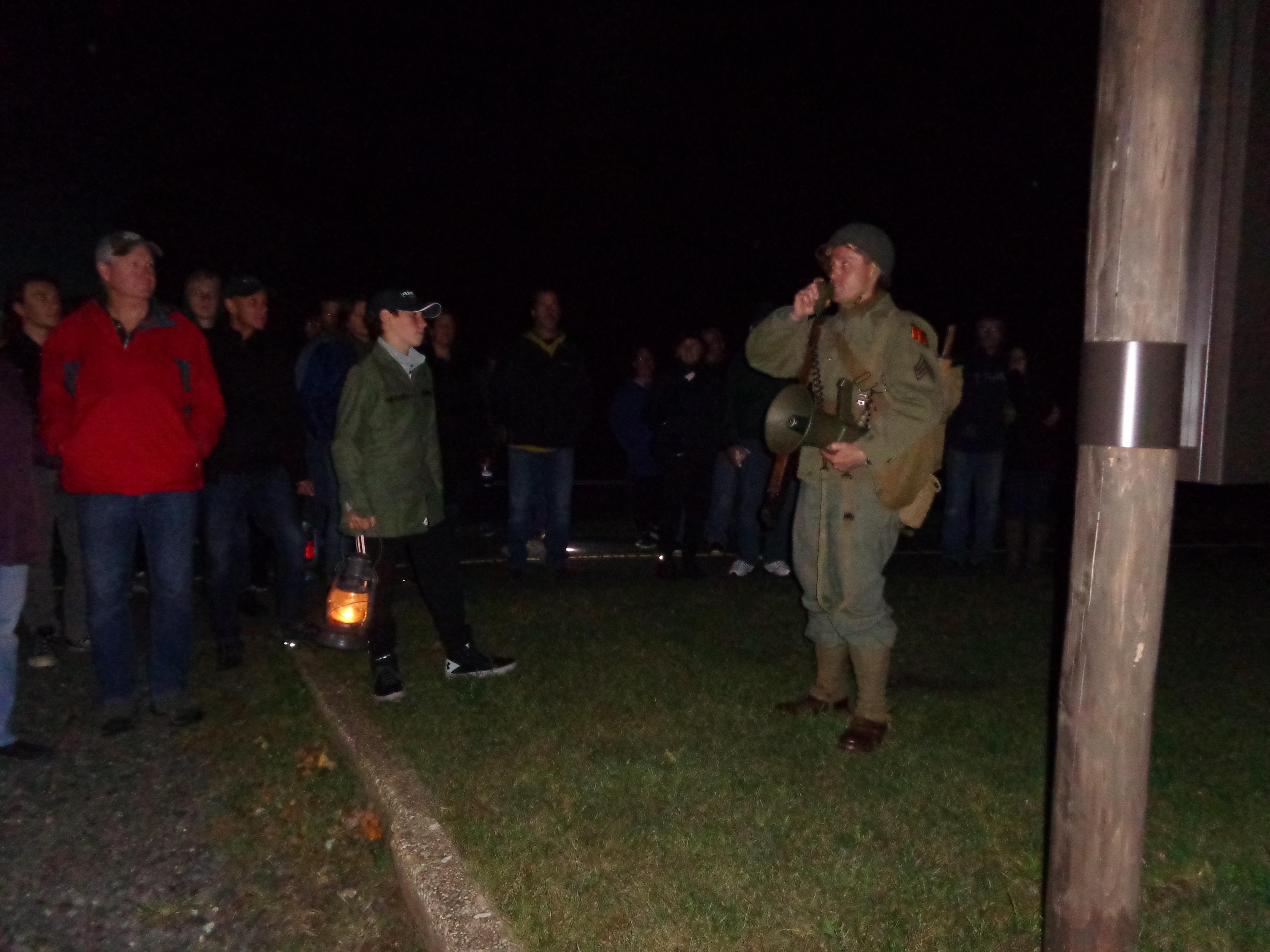 Man in WW II military uniform leading group of visitors holding lanterns