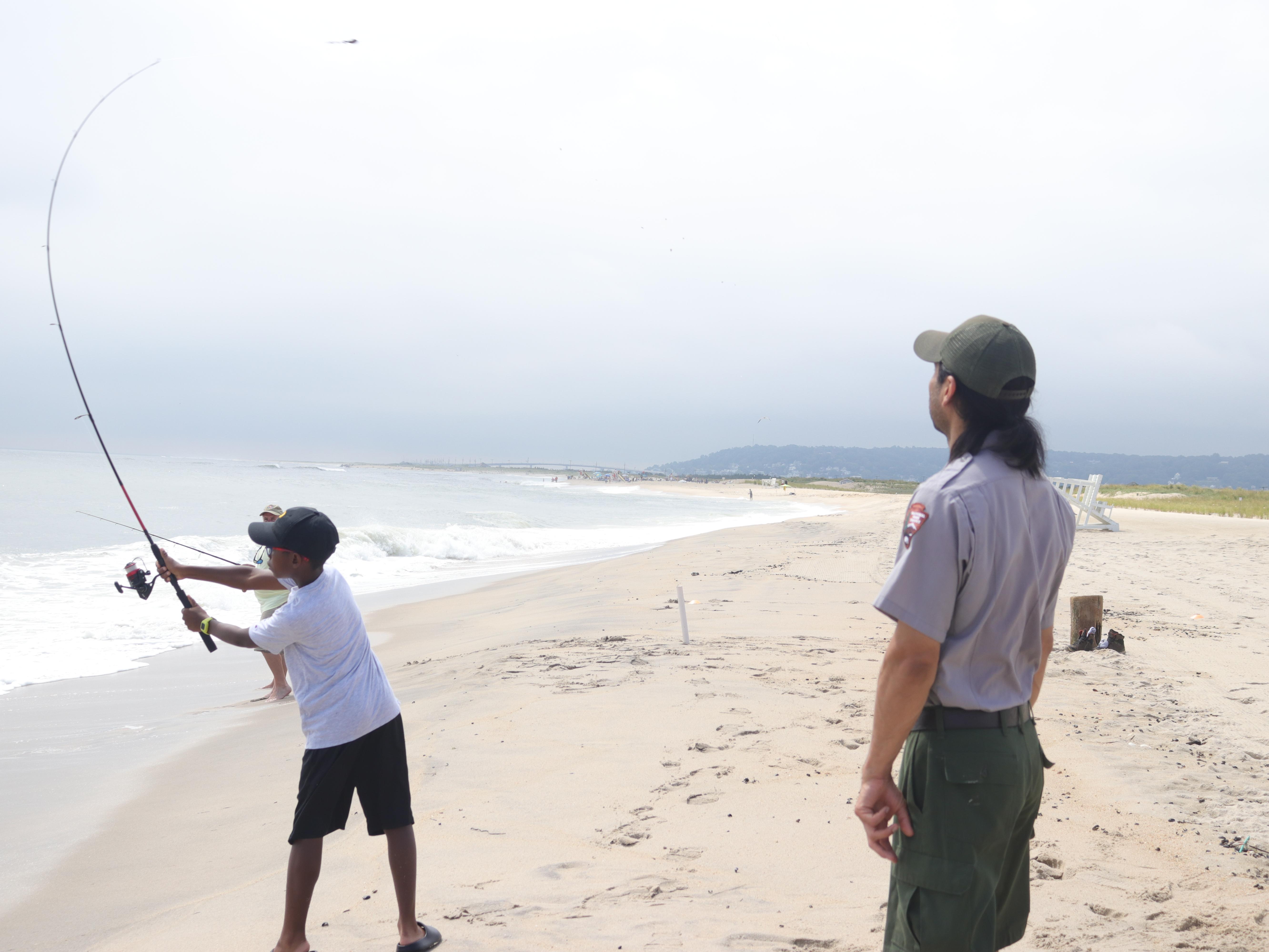Child casting fishing rod being watched by park ranger