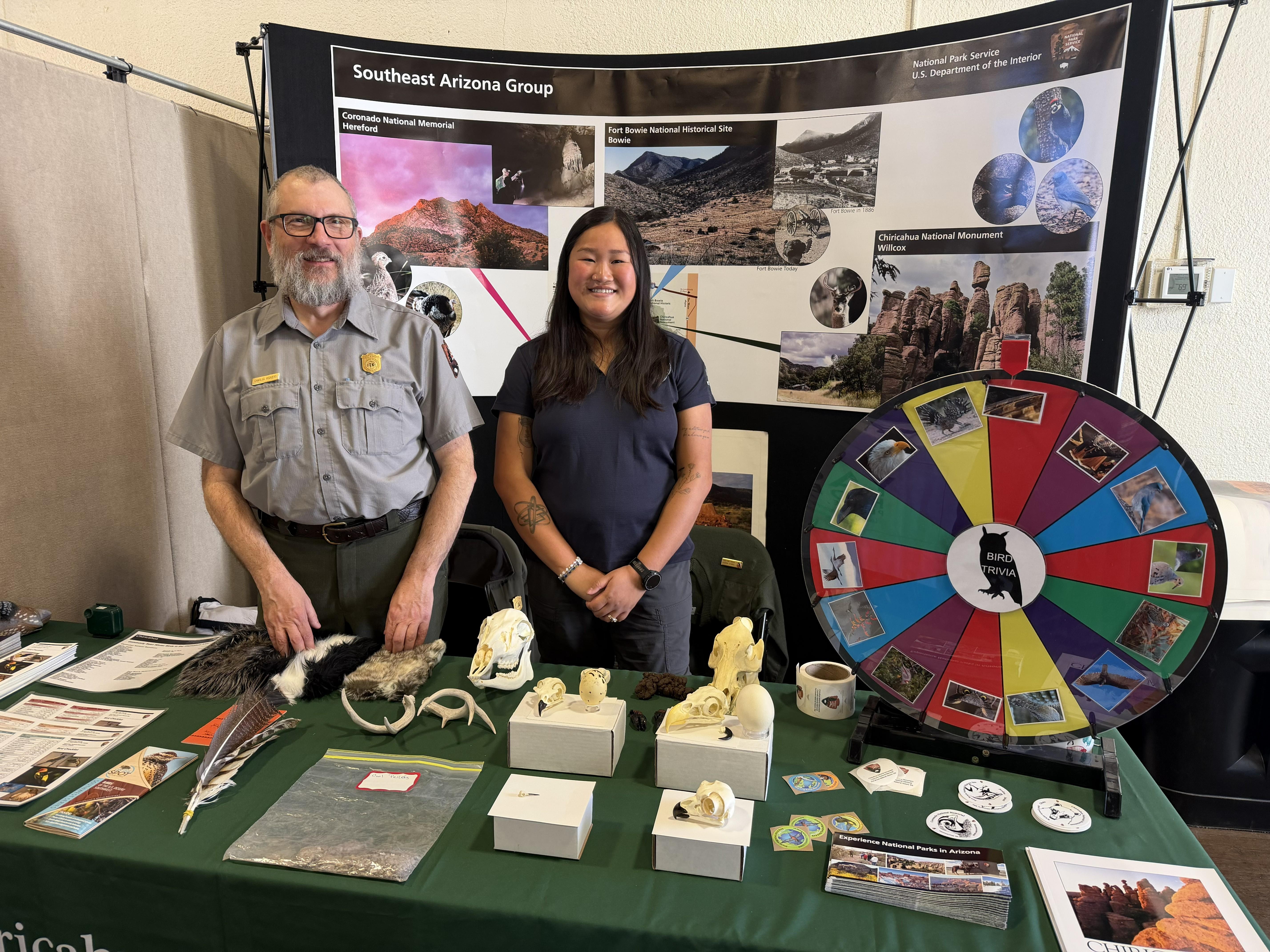 ranger and intern stand at booth with wildlife trivia wheel