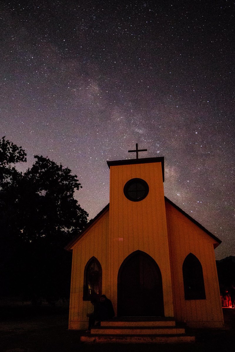 Starry night sky with white church in the foreground.