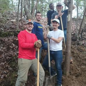 A group of men standing along trail with work gear on.