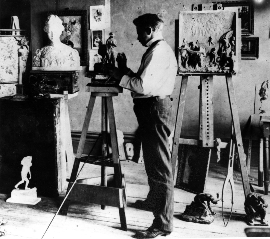 A black and white photo of a man molding a sculpture in a studio