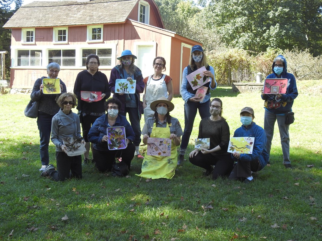 A group of people holding up their art in a grassy meadow.