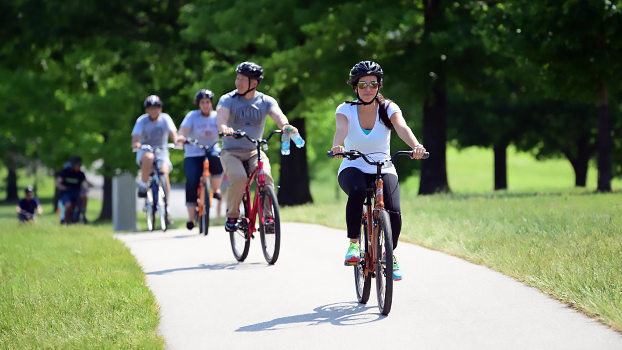 four smiling people wearing helmets riding bicycles on a paved path