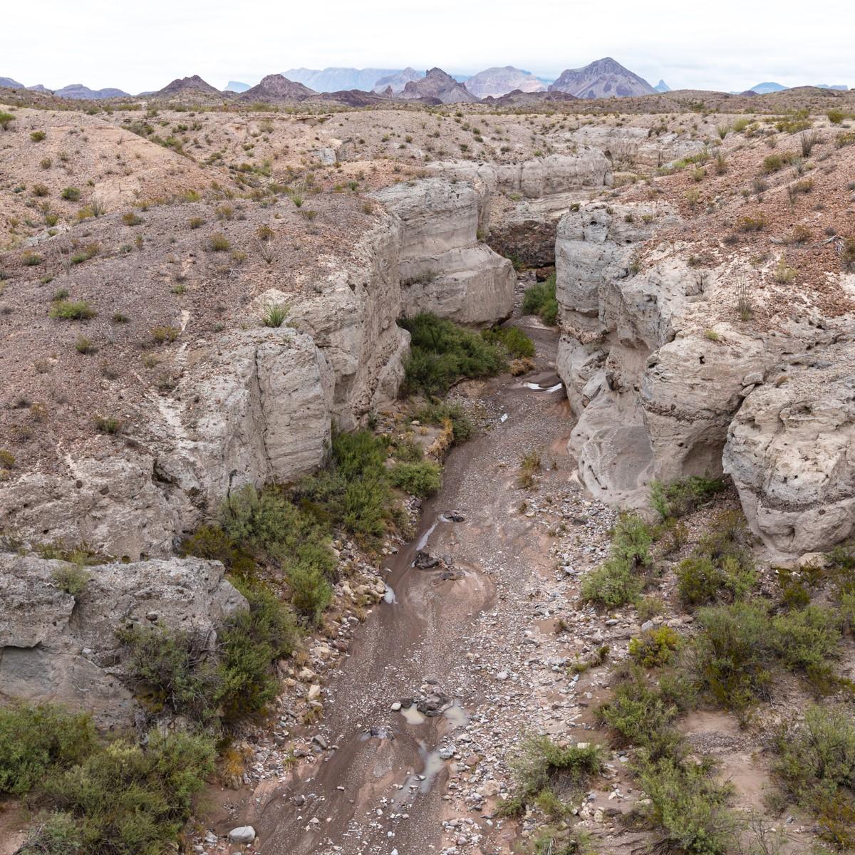 A deep, sand-bottomed canyon flanked by light-colored ash walls.