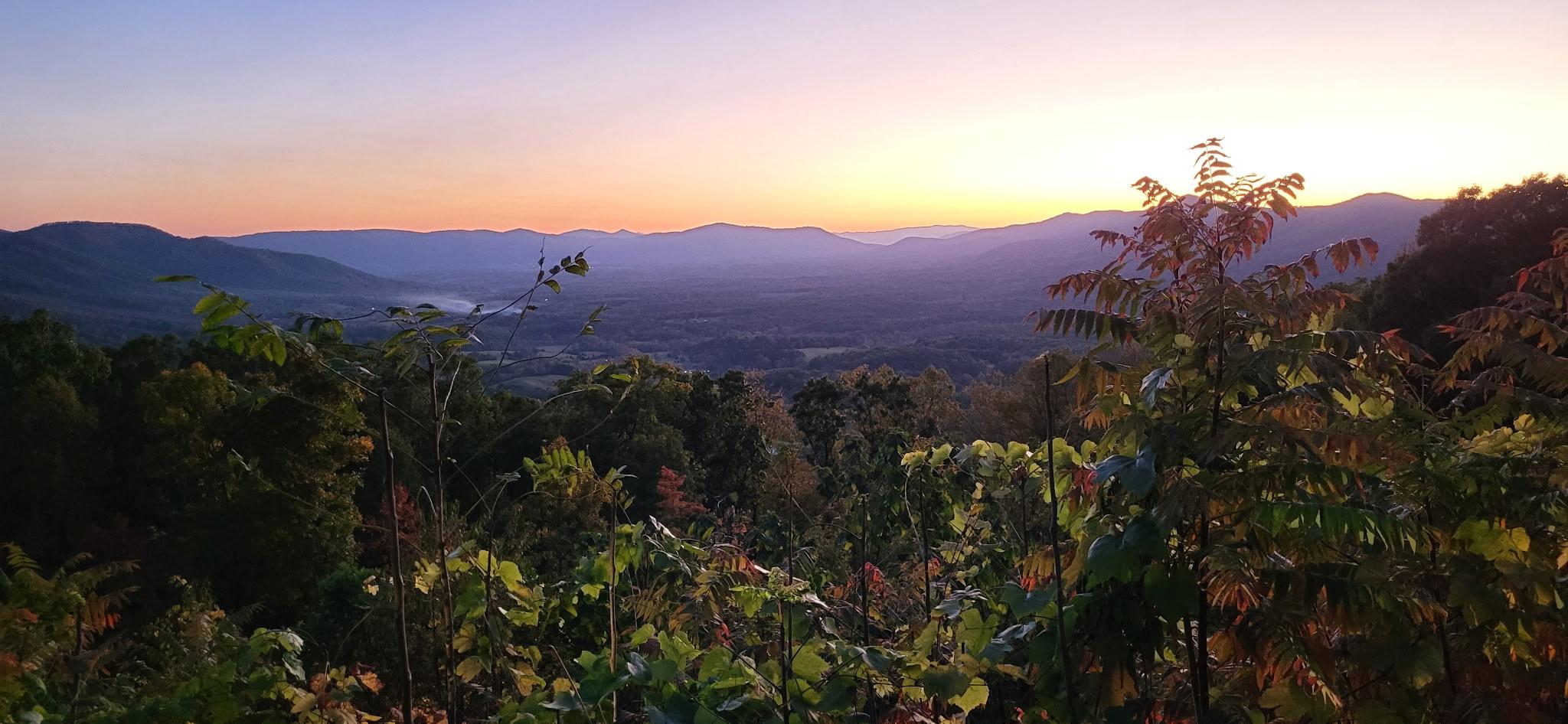 sunrise skies over mountains with trees in the foreground