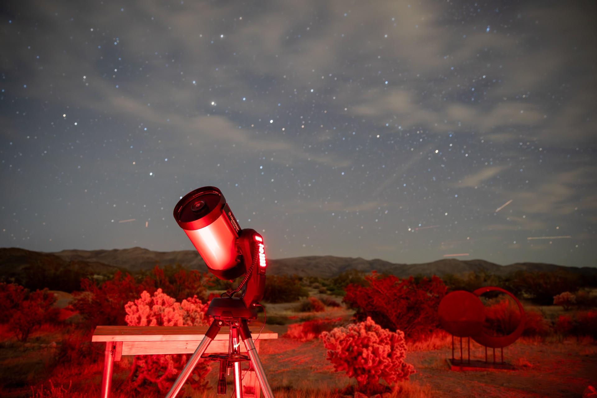 A telescope, bathed in red light, with the night sky behind it