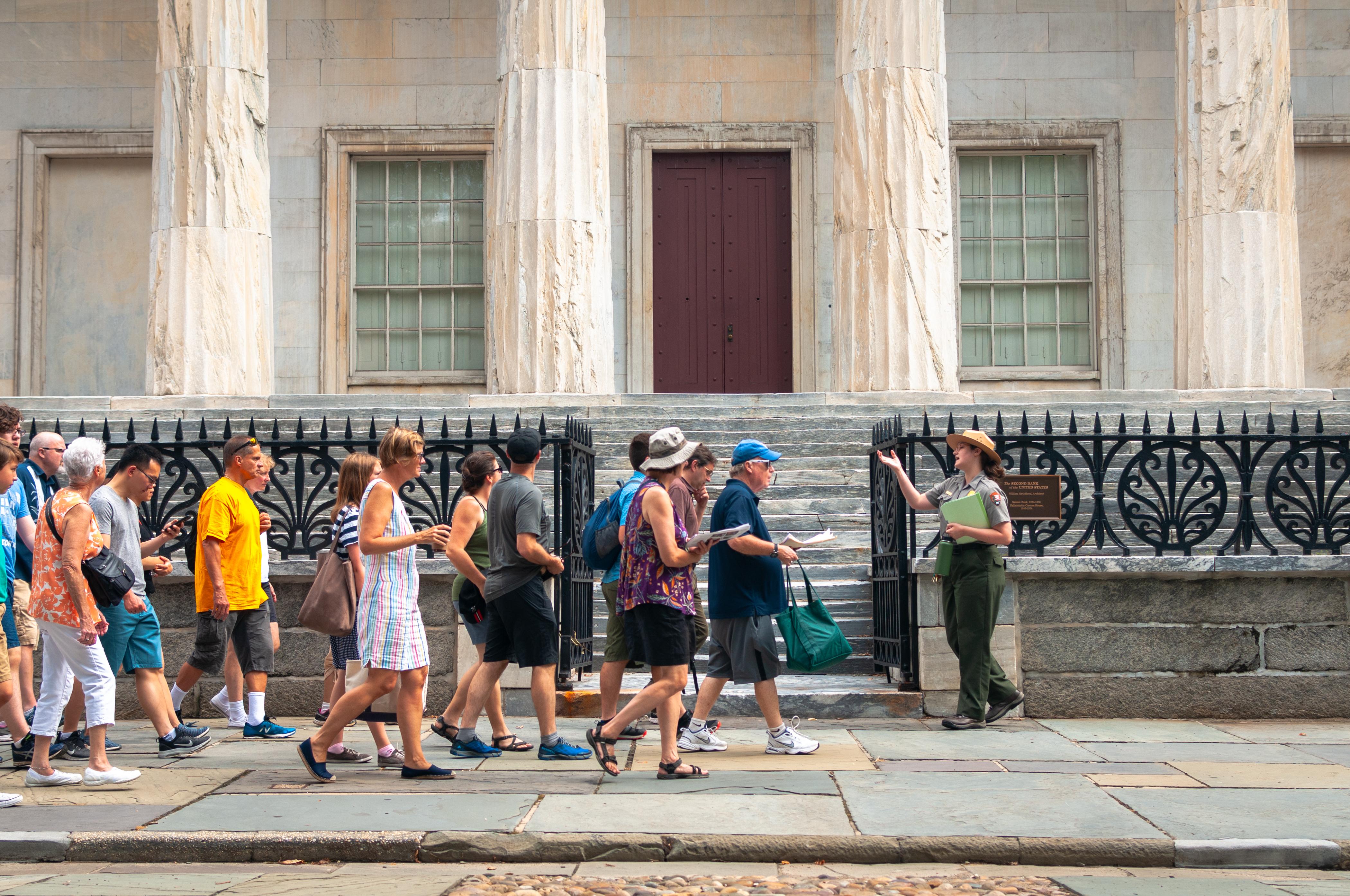 A park ranger leading a group of visitors past an historic marble building.