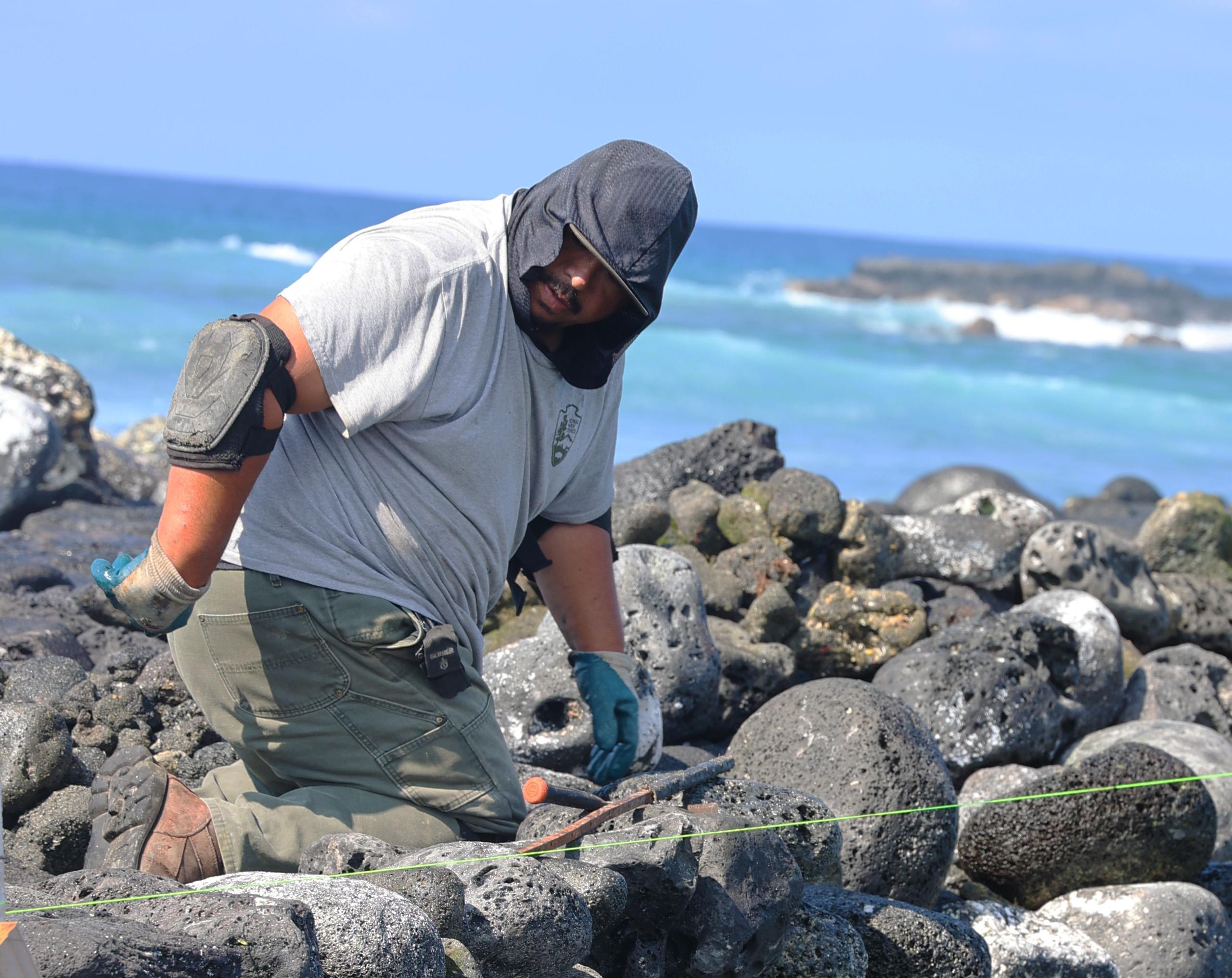 National Park Service employee moving large stones on rock wall with ocean in the background