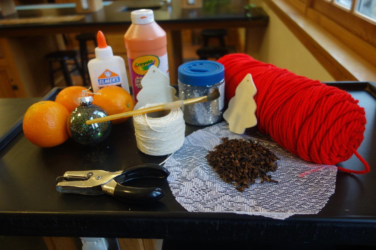 Red yarn, oranges, lace, cloves, string, glitter, glue, orange paint, one wooden tree, hole punch.