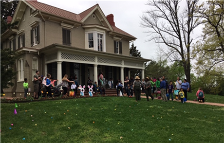Young children, parents, and rangers gather in front of historic home