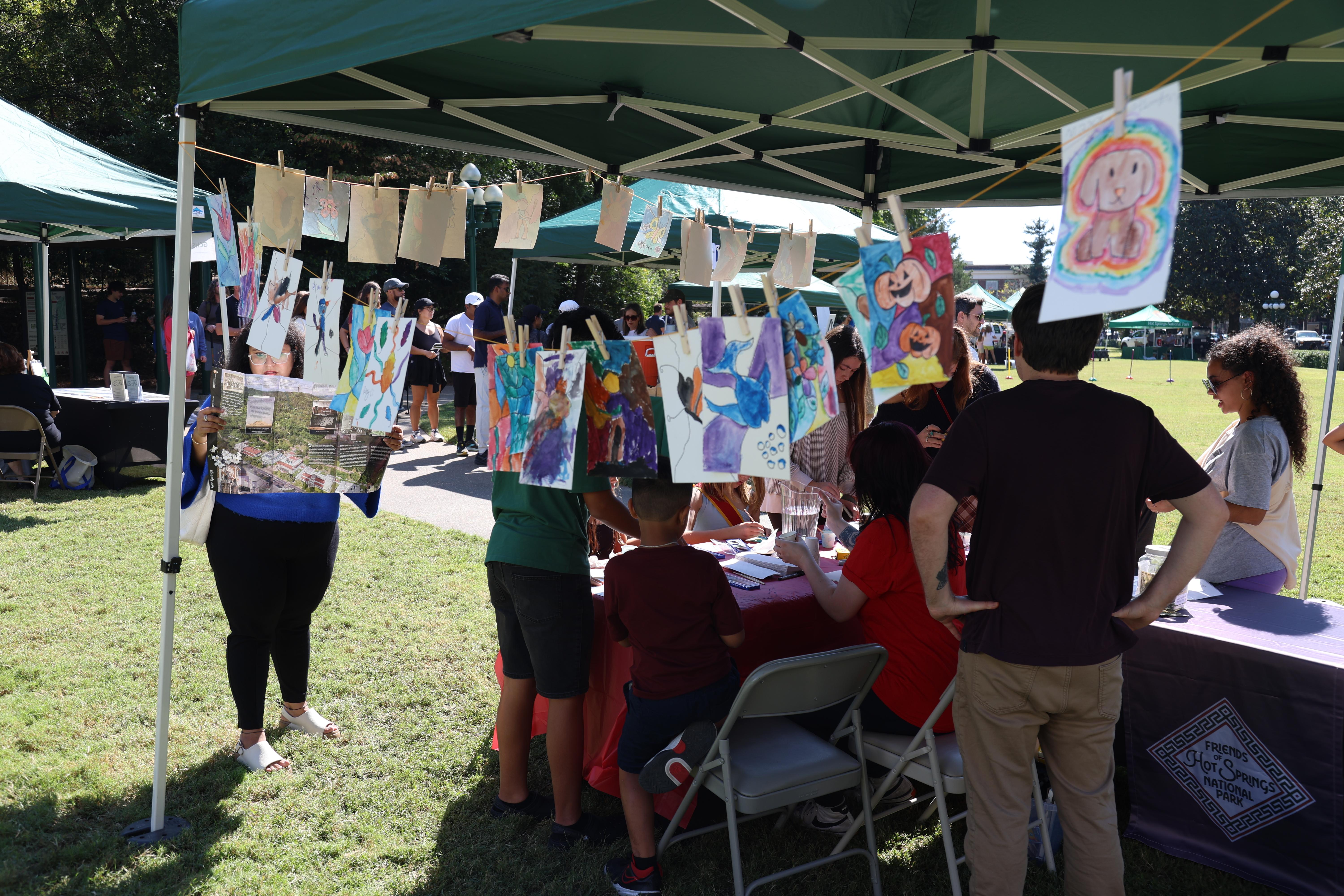 Examples of water color art hang from a string while a group of people gather in the background.