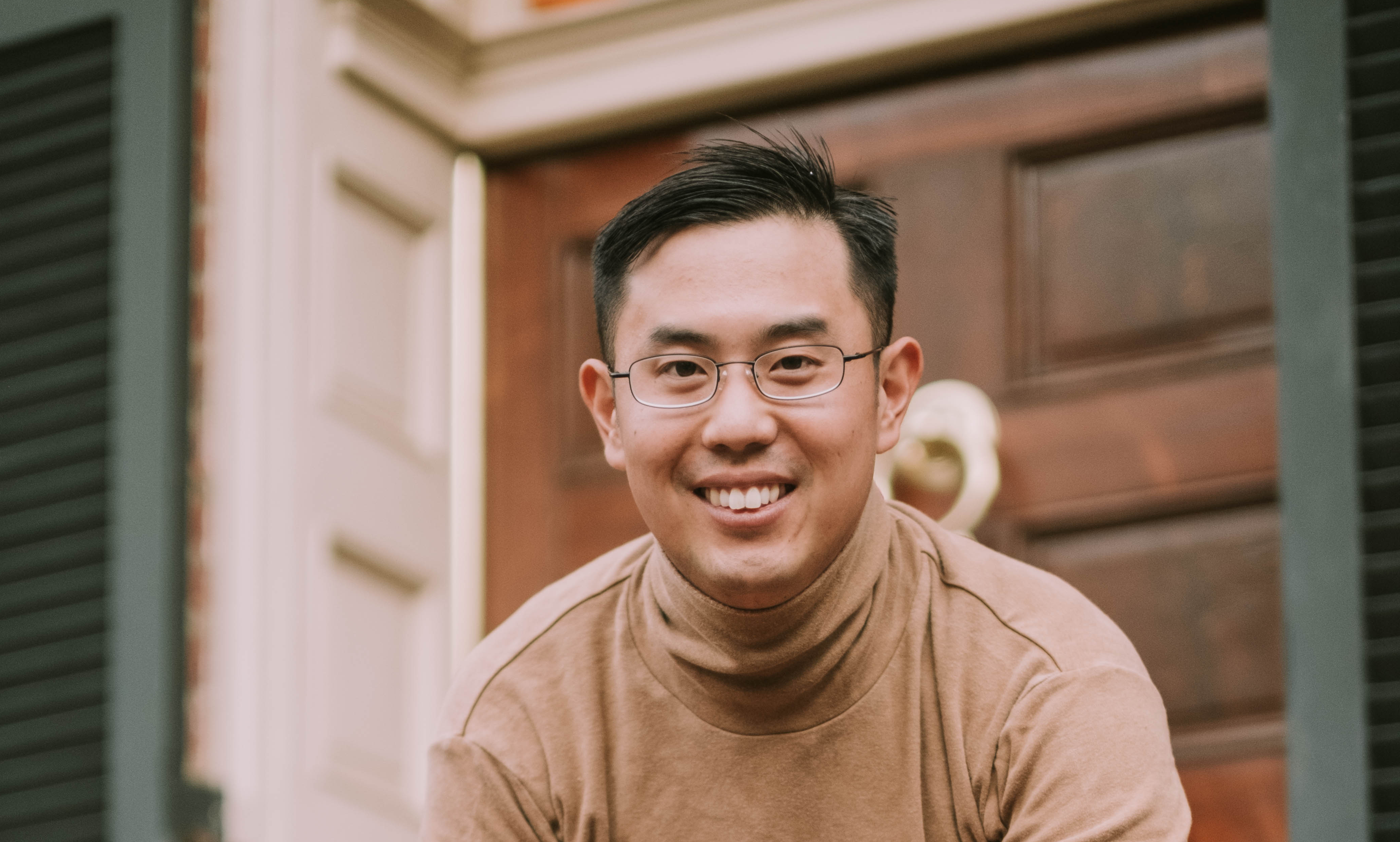 Asian American Man leaning on a fence smiling