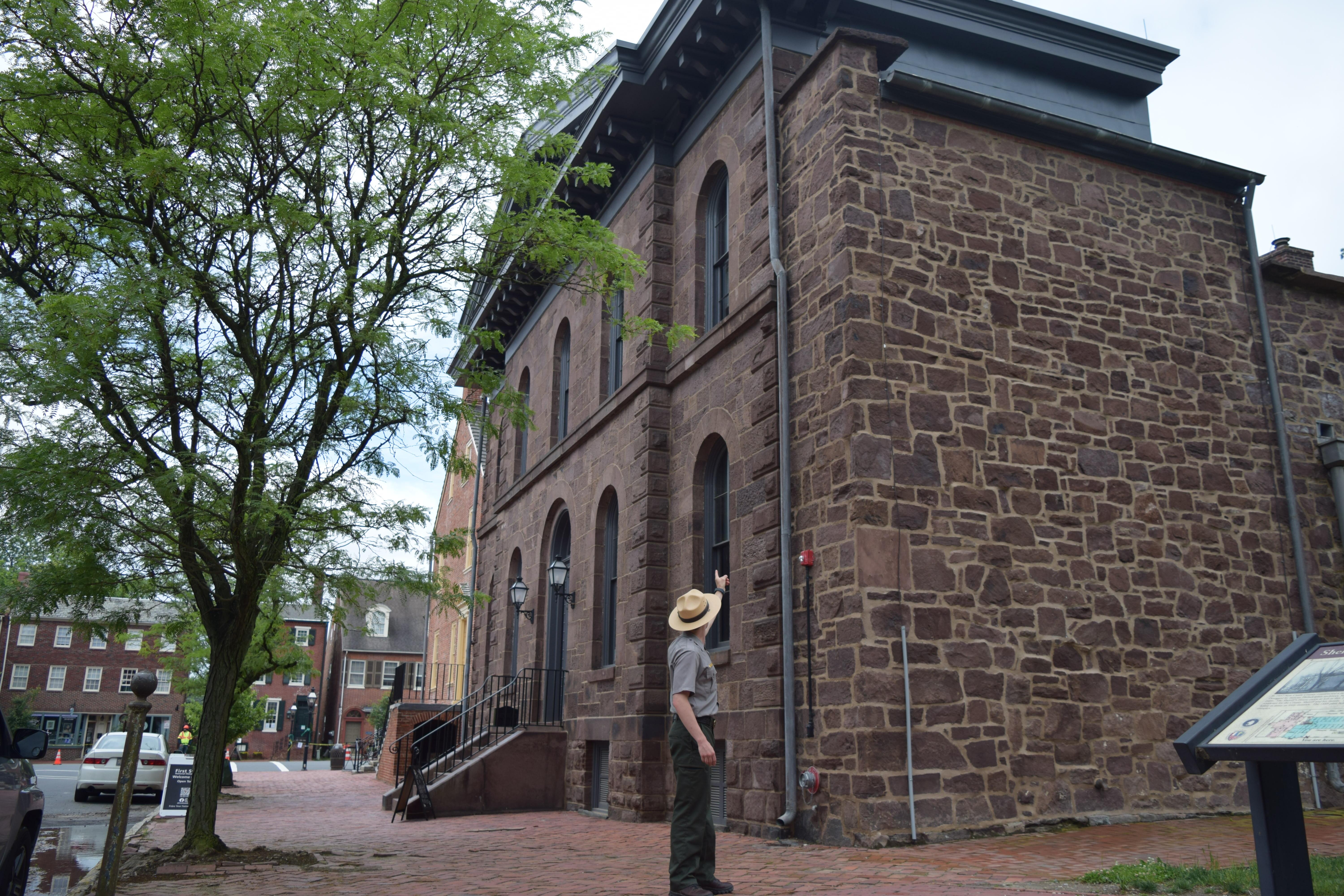 A ranger points at a brown brick building.