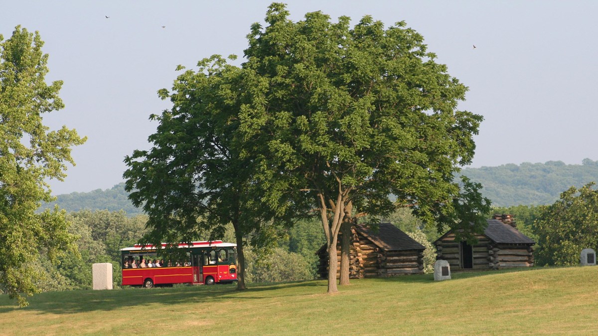a trolley drives past log huts and monuments