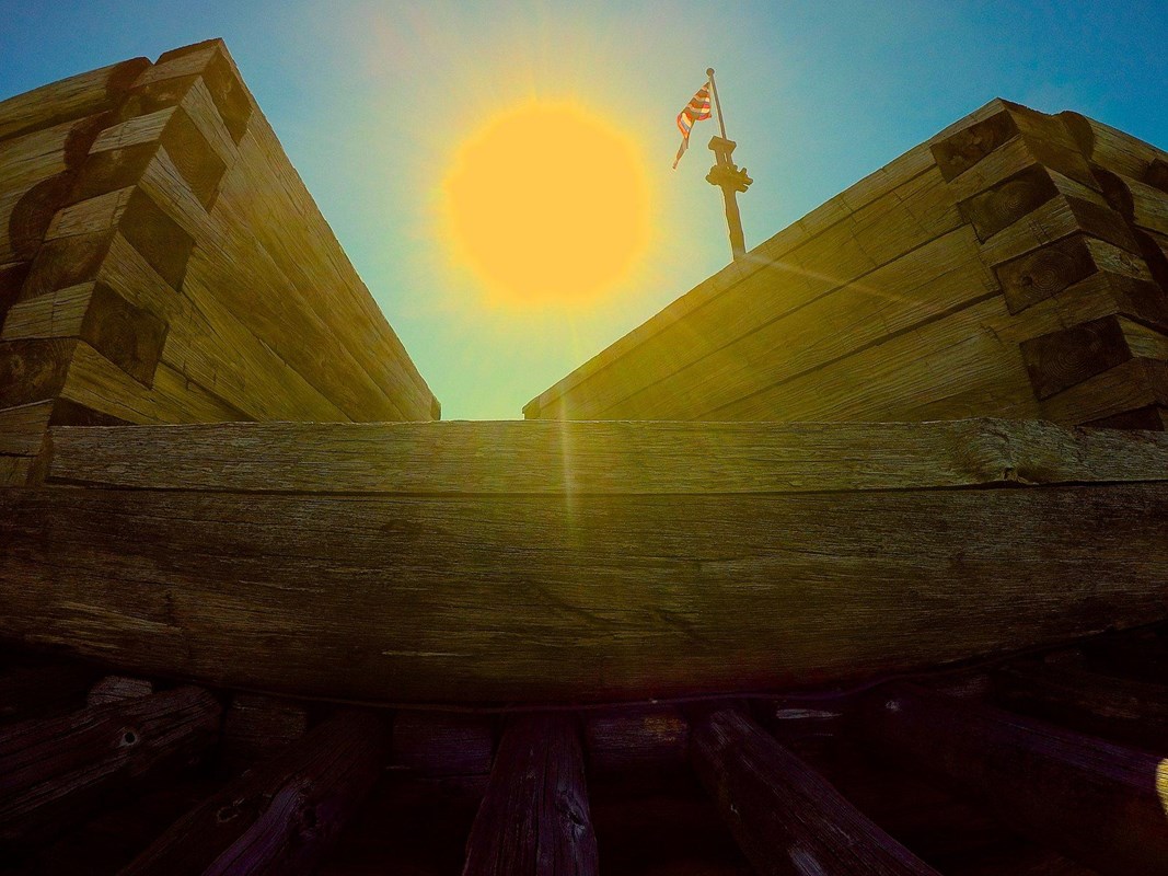 Looking through a break in the fort wall, the flag flies and a LARGE sun floats in the sky.