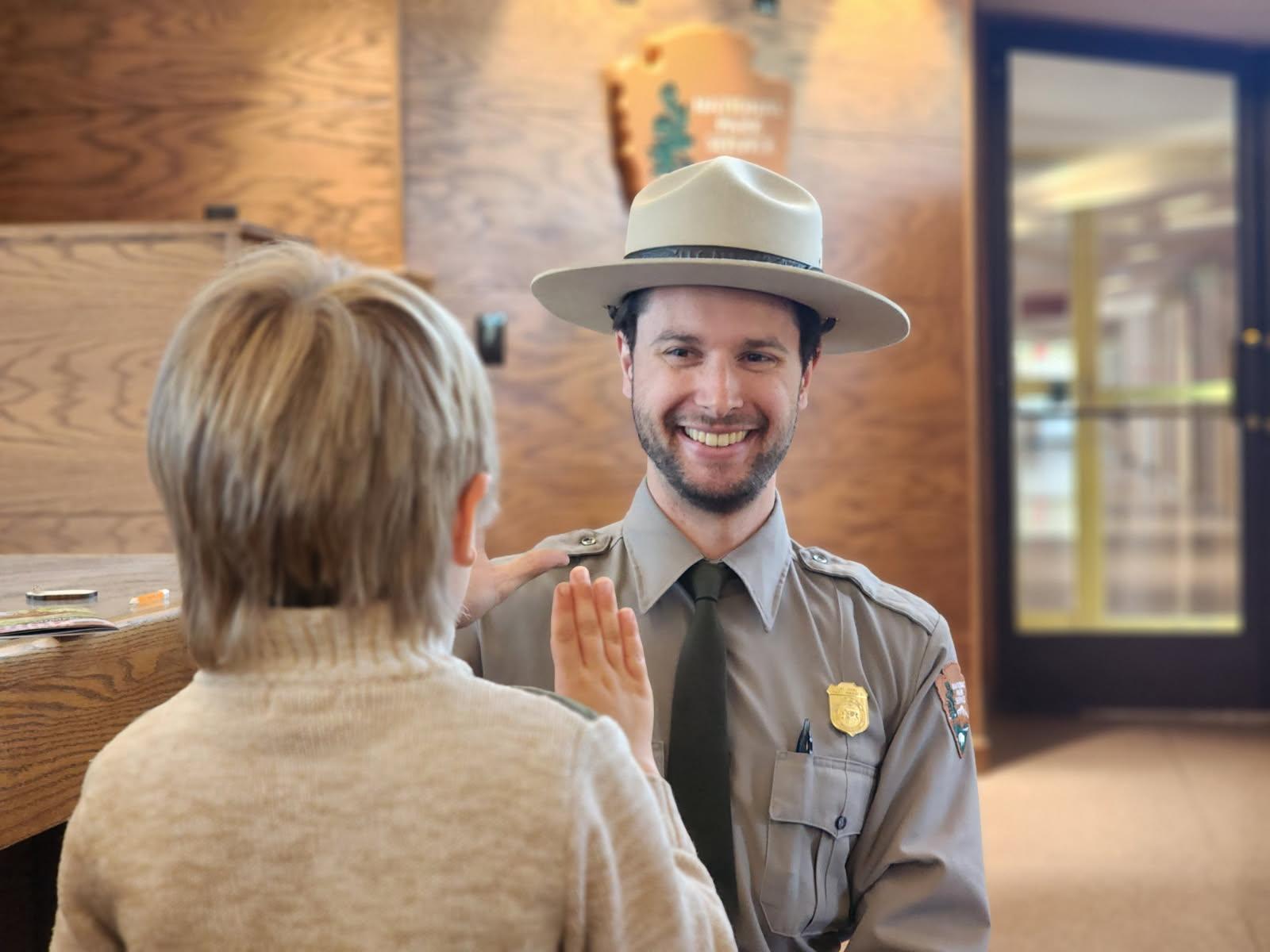 A park ranger has his hand raised and is swearing in a new Junior Ranger