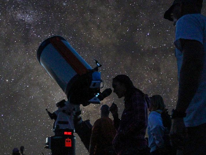 Beneath the Milky Way Galaxy, several people are looking through telescopes.