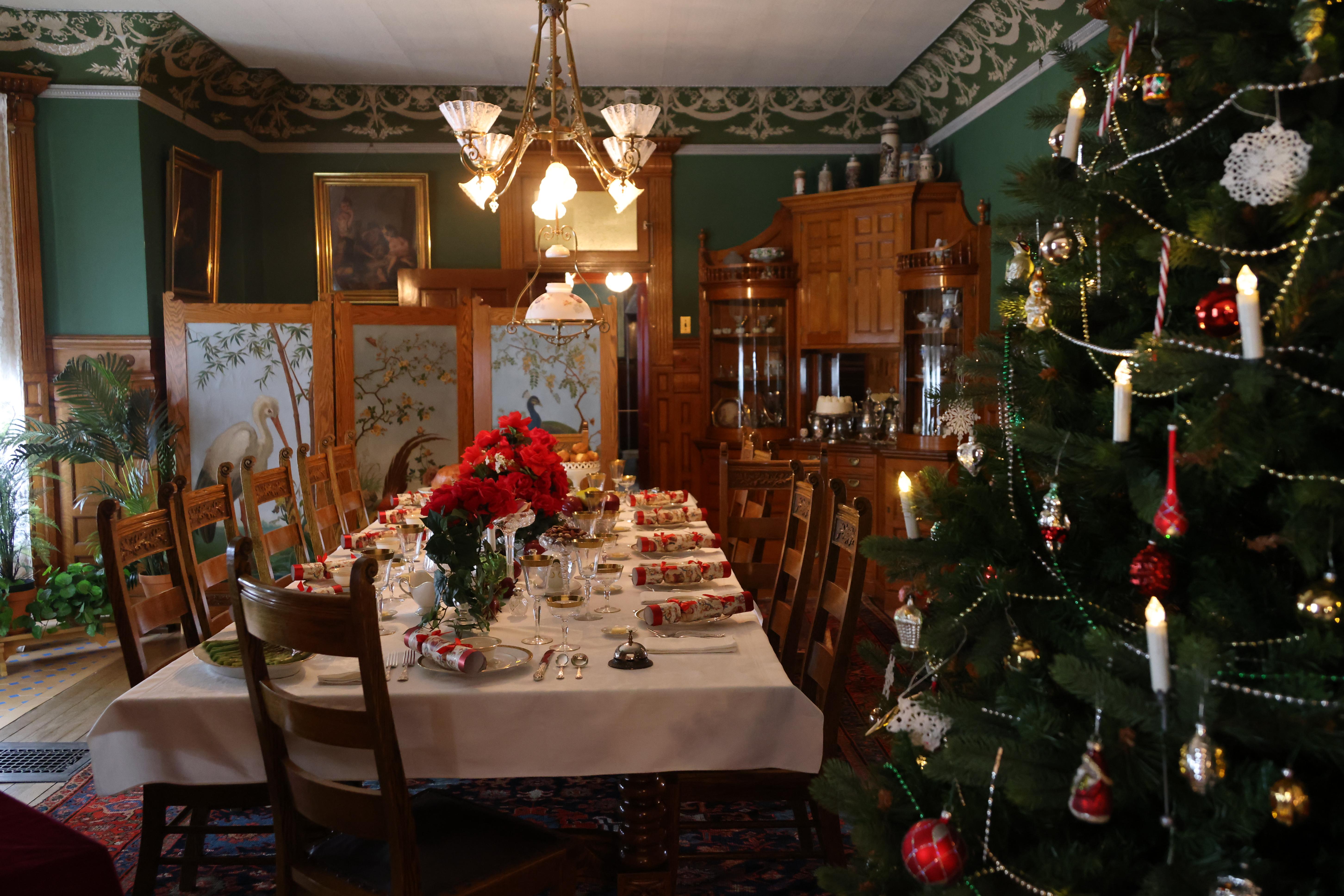 A large dining room with a set table and a Christmas tree in the right hand corner