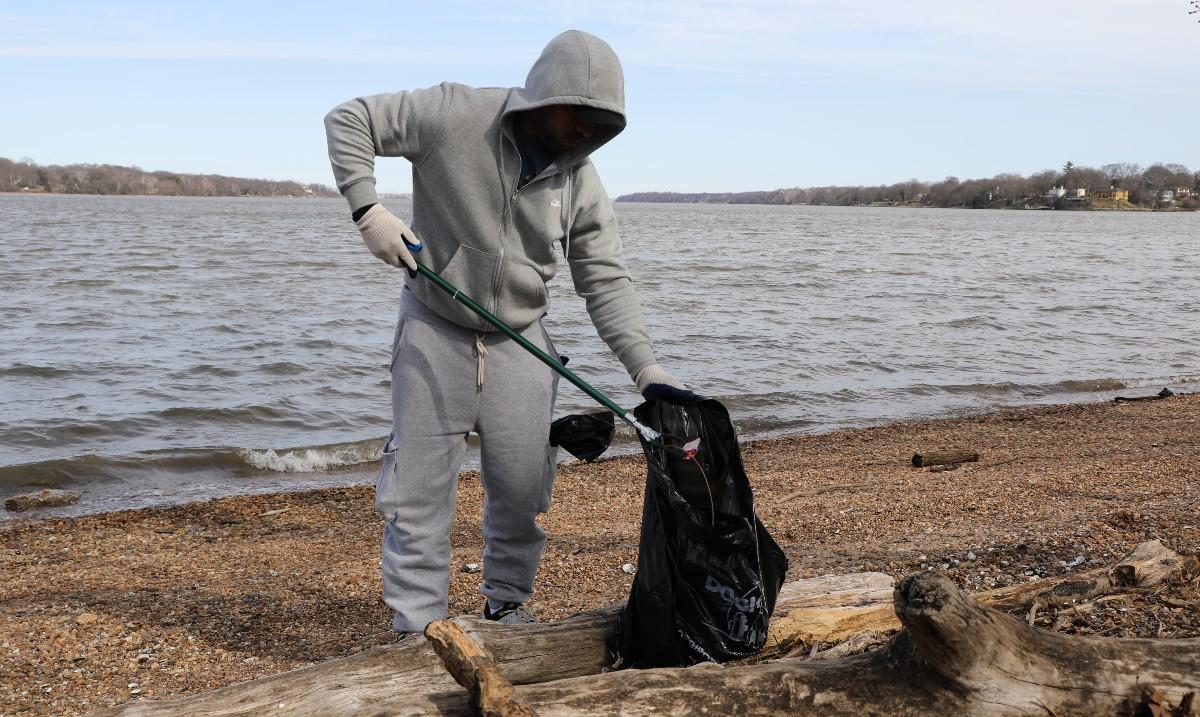 A volunteer on the shoreline picking up trash with the river in the background