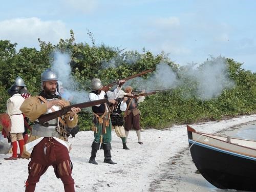 re-enactors dressed as conquistadores fire muskets on a beach.
