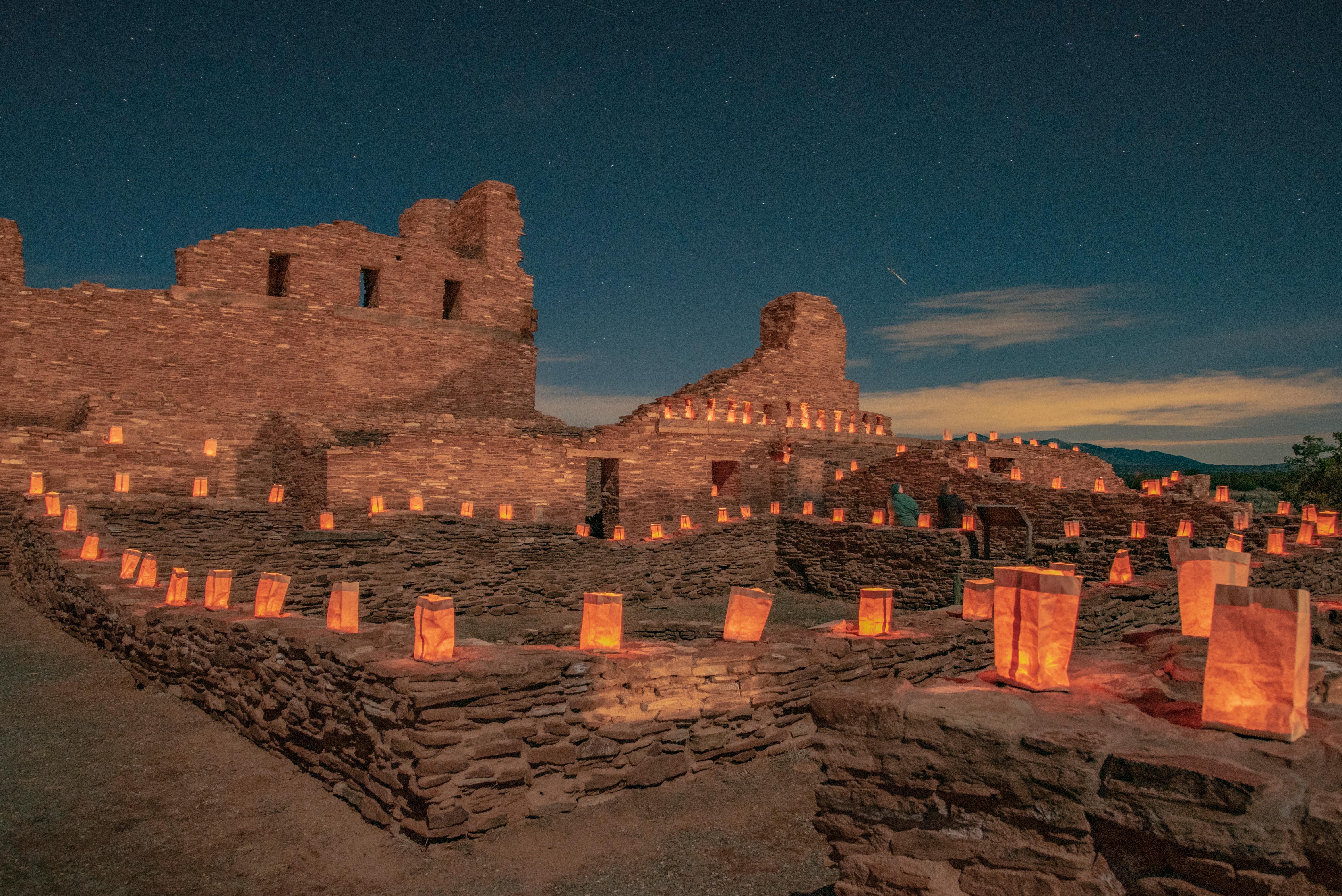 Hundreds of glowing luminarias lining the stone walls of a historic church at dusk.