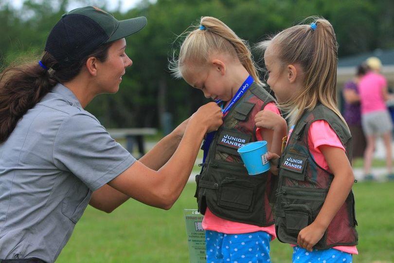 park ranger pins a badge on one girl. Another girl wearing a vest stands next to her.