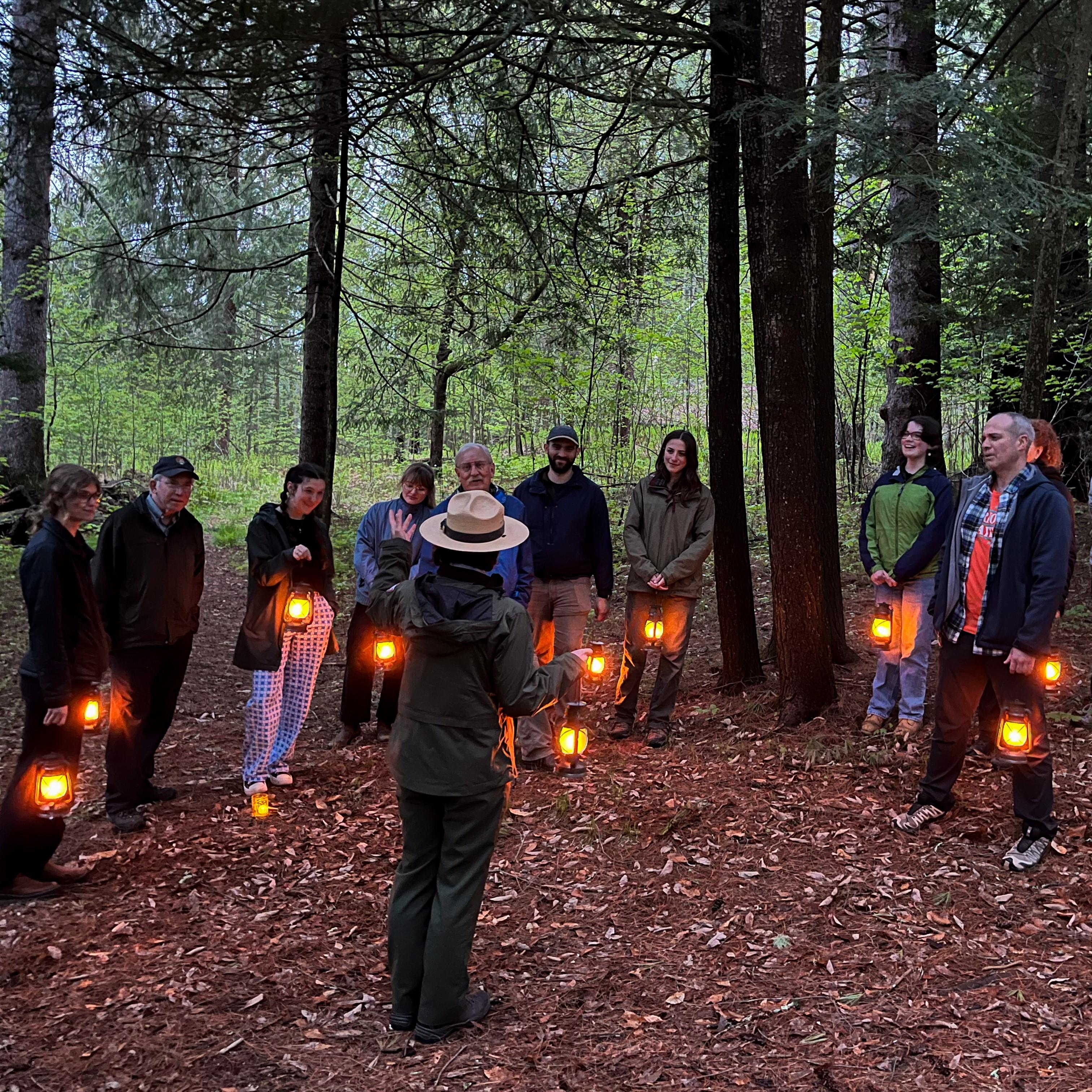 Park Ranger talks to a group of visitors in the forest at dusk, all are holding lanterns