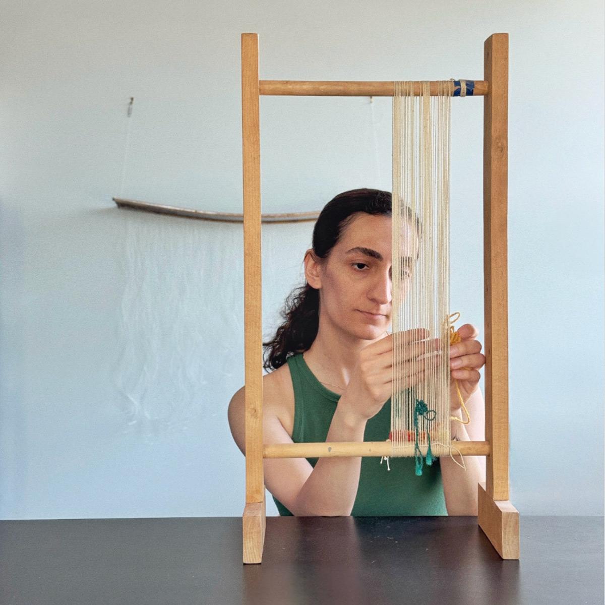 Artist-in-Residence Zara Shahi works on a small tabletop loom while weaving within thread.