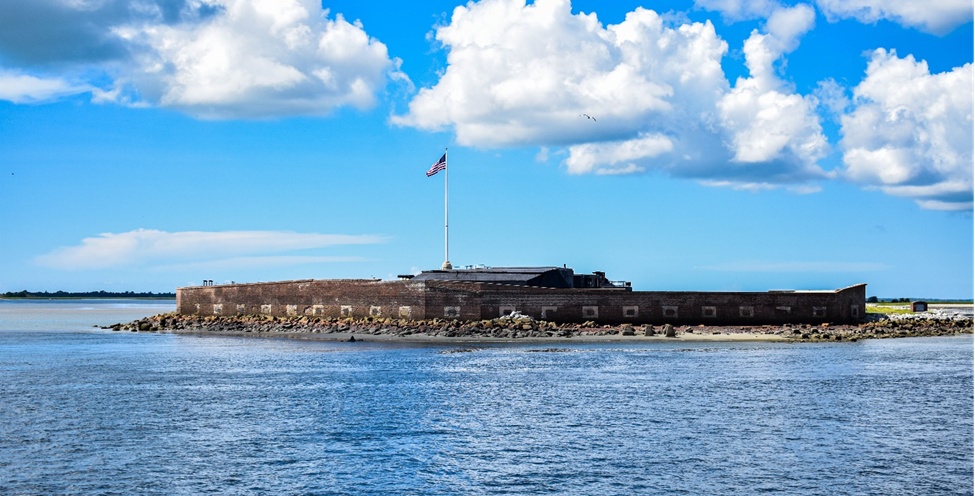 Fort Sumter, and island, on a bright day. Puffy clouds are in the sky. The American flag is flying.