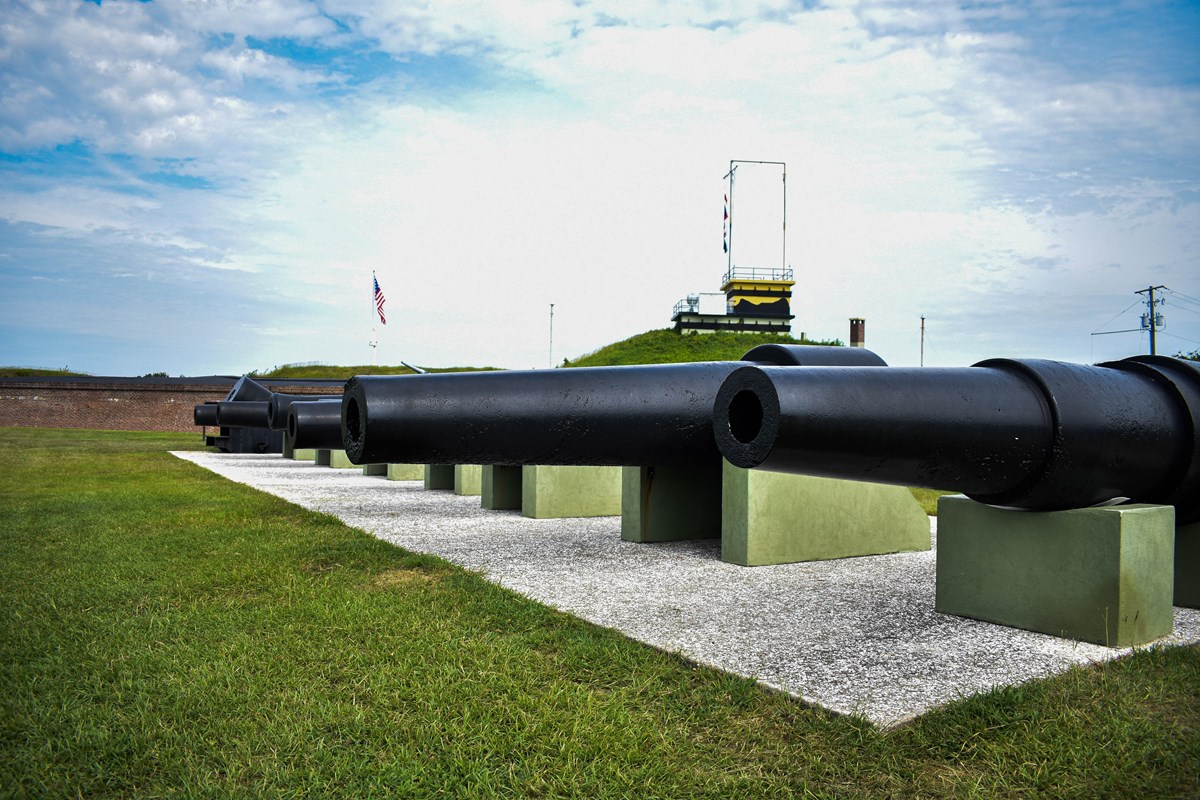 Several historic cannons at Fort Moultrie, lined up in a row. Behind them is the historic fort.