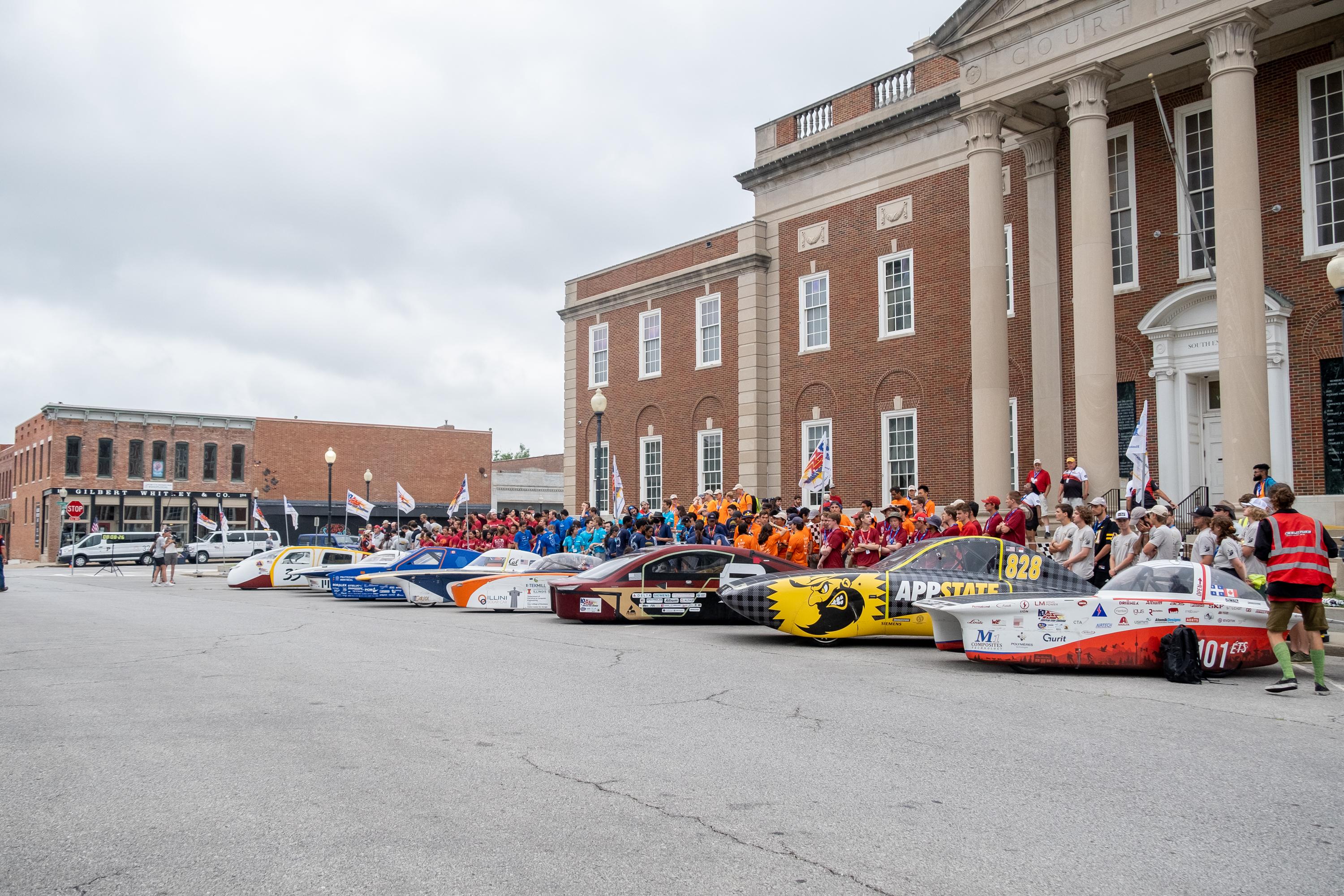 Solar cars with people standing around them.