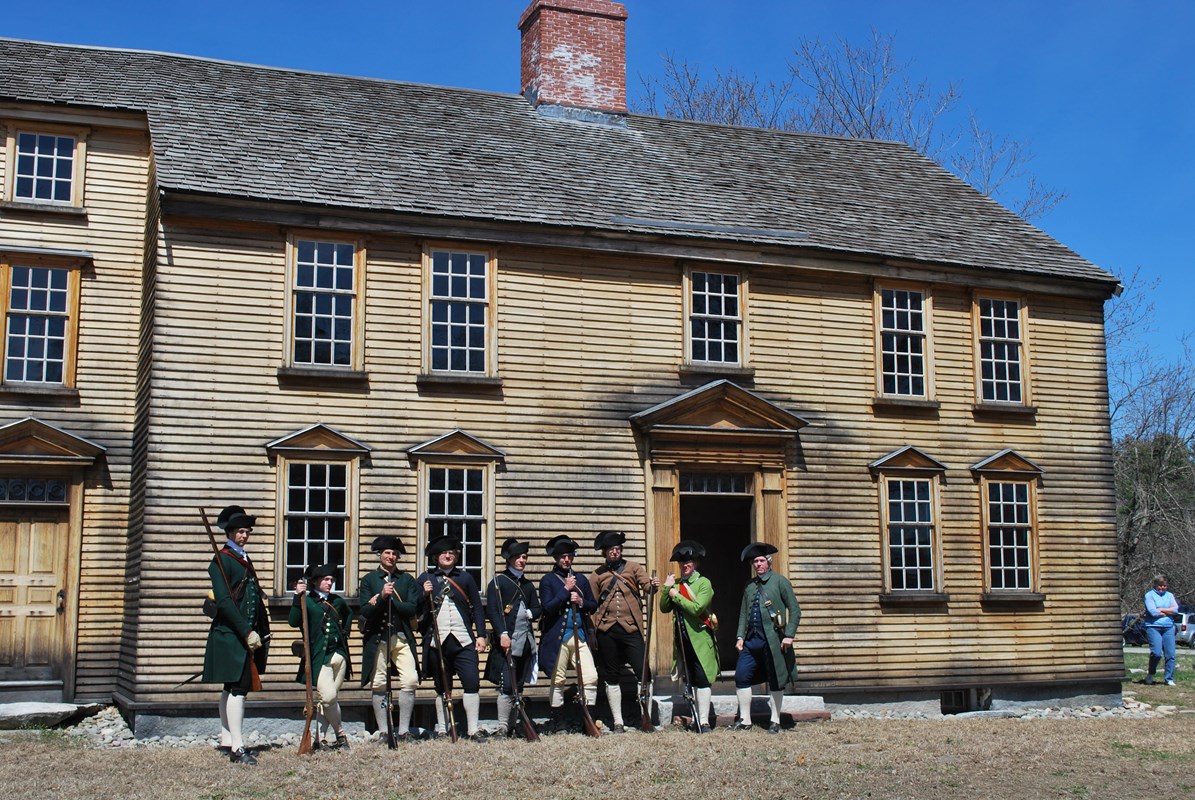Two story wooden colonial house with people dressed in 18th century clothing in front