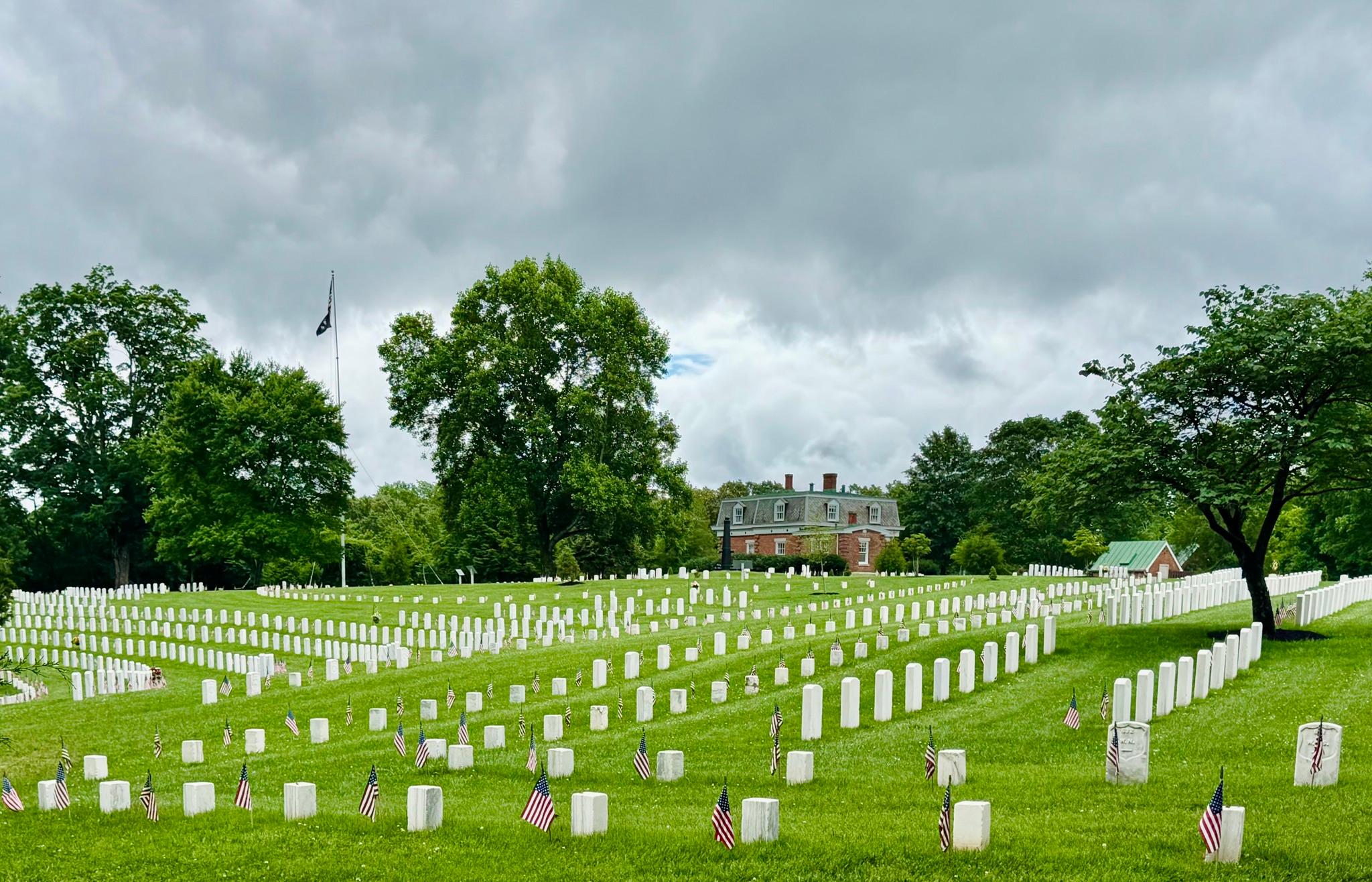A green, sloping national cemetery filled with rows of white headstones and small American flags str
