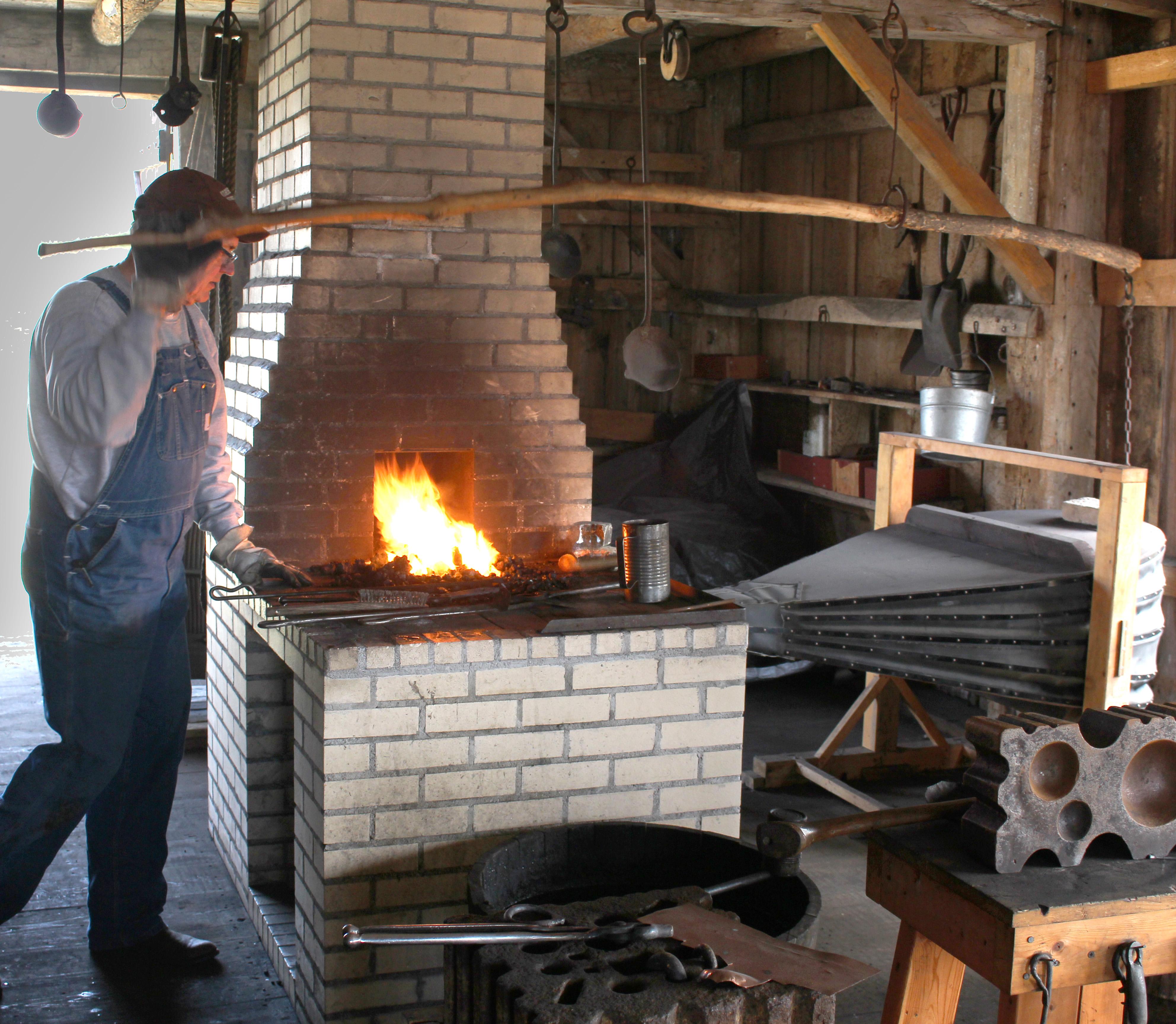 A man stands over a brick hearth inside a building