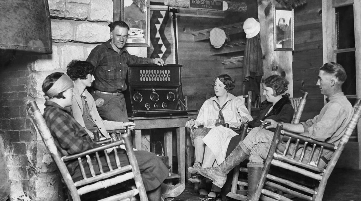 A black and white photo of a group of people standing around a historic radio