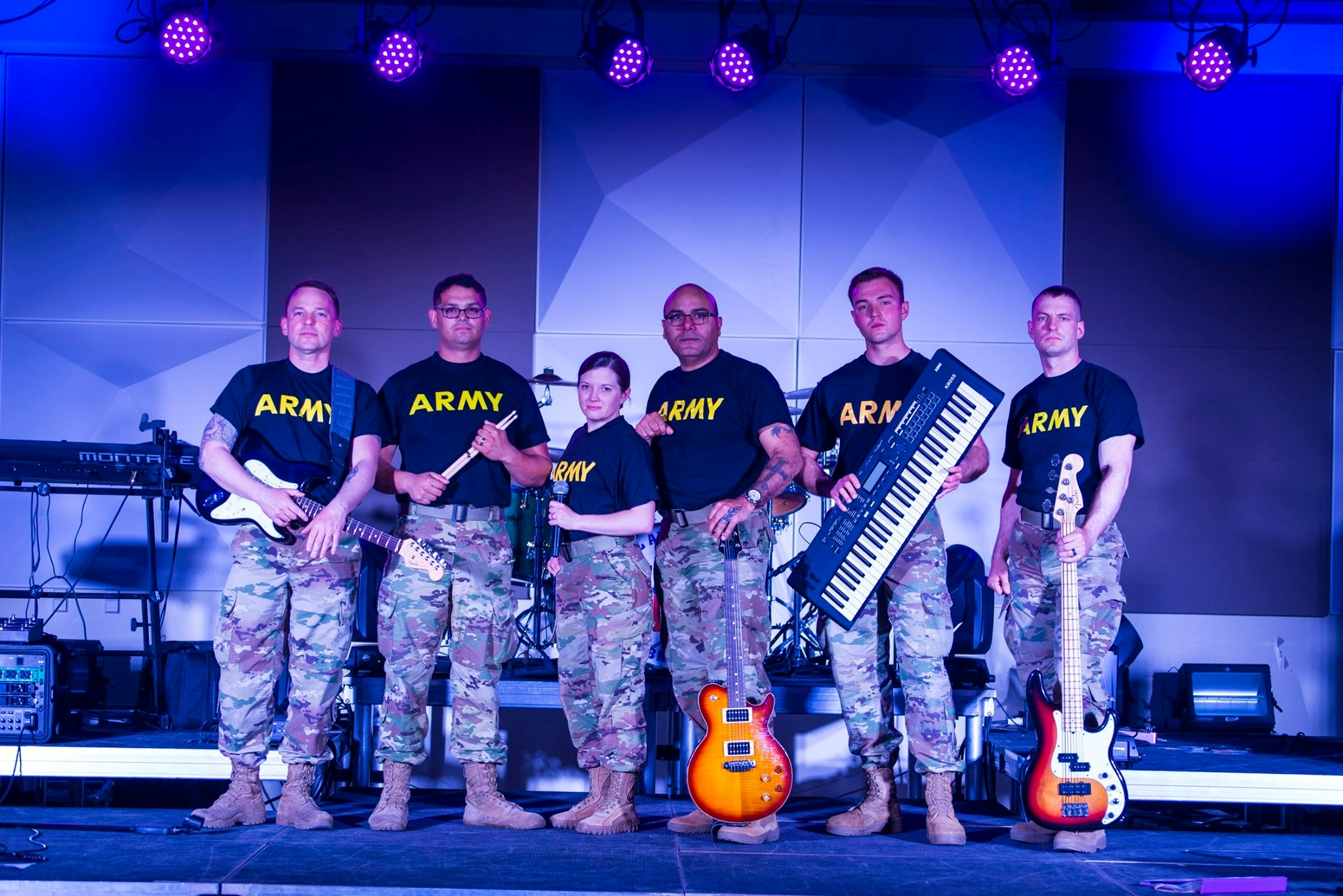 Six figures in military uniforms stand on a stage holding their musical instruments.