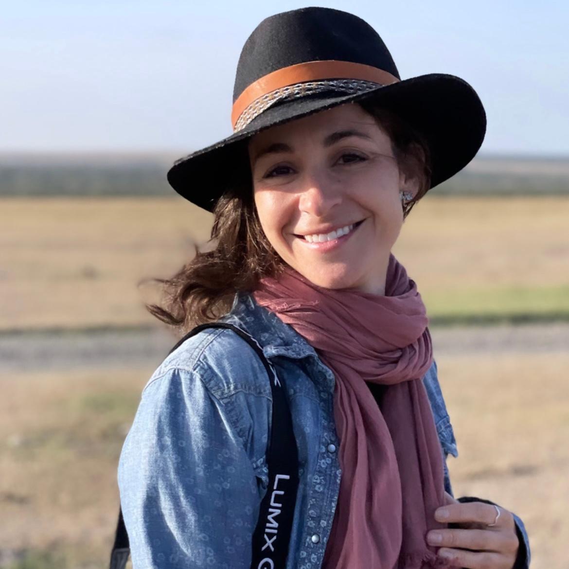 a headshot image of woman wearing a hat, denim shirt, and a scarf