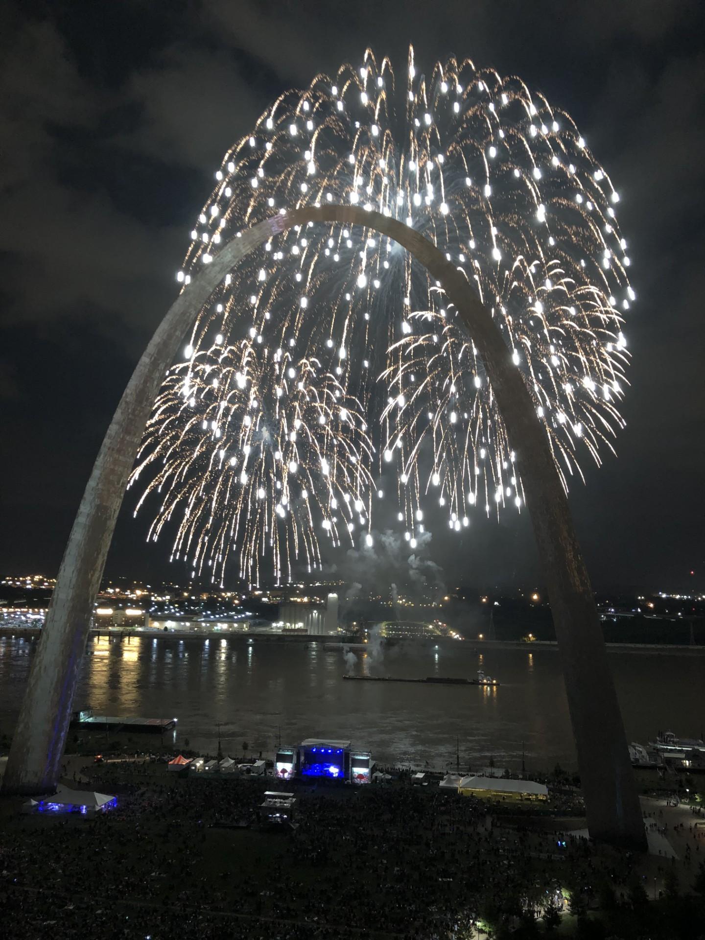 fireworks against the night sky with the silhouette of the Gateway Arch against the glow
